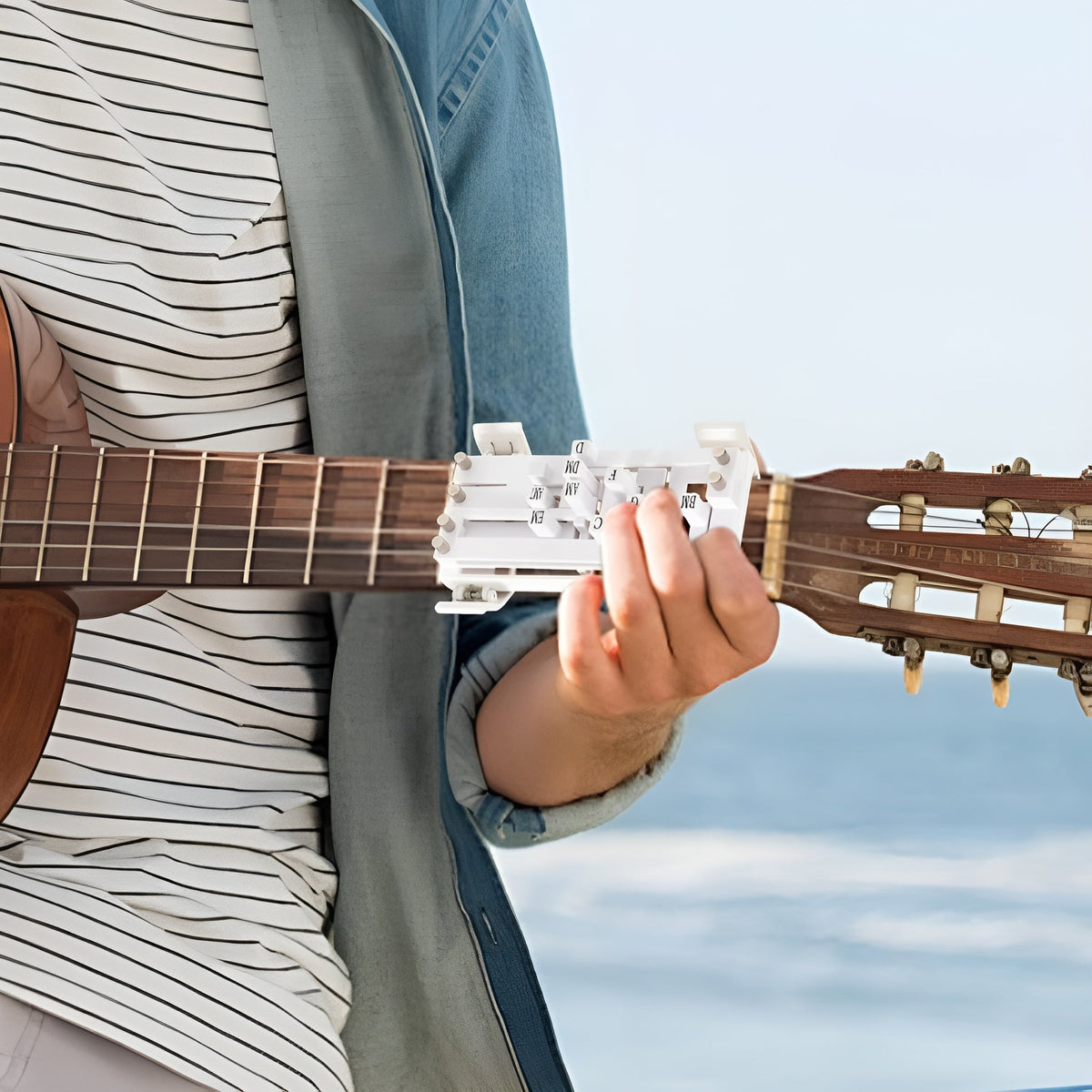 Aide aux accords Accordino blanche clipsée sur le manche d'une guitare, au bord de la mer