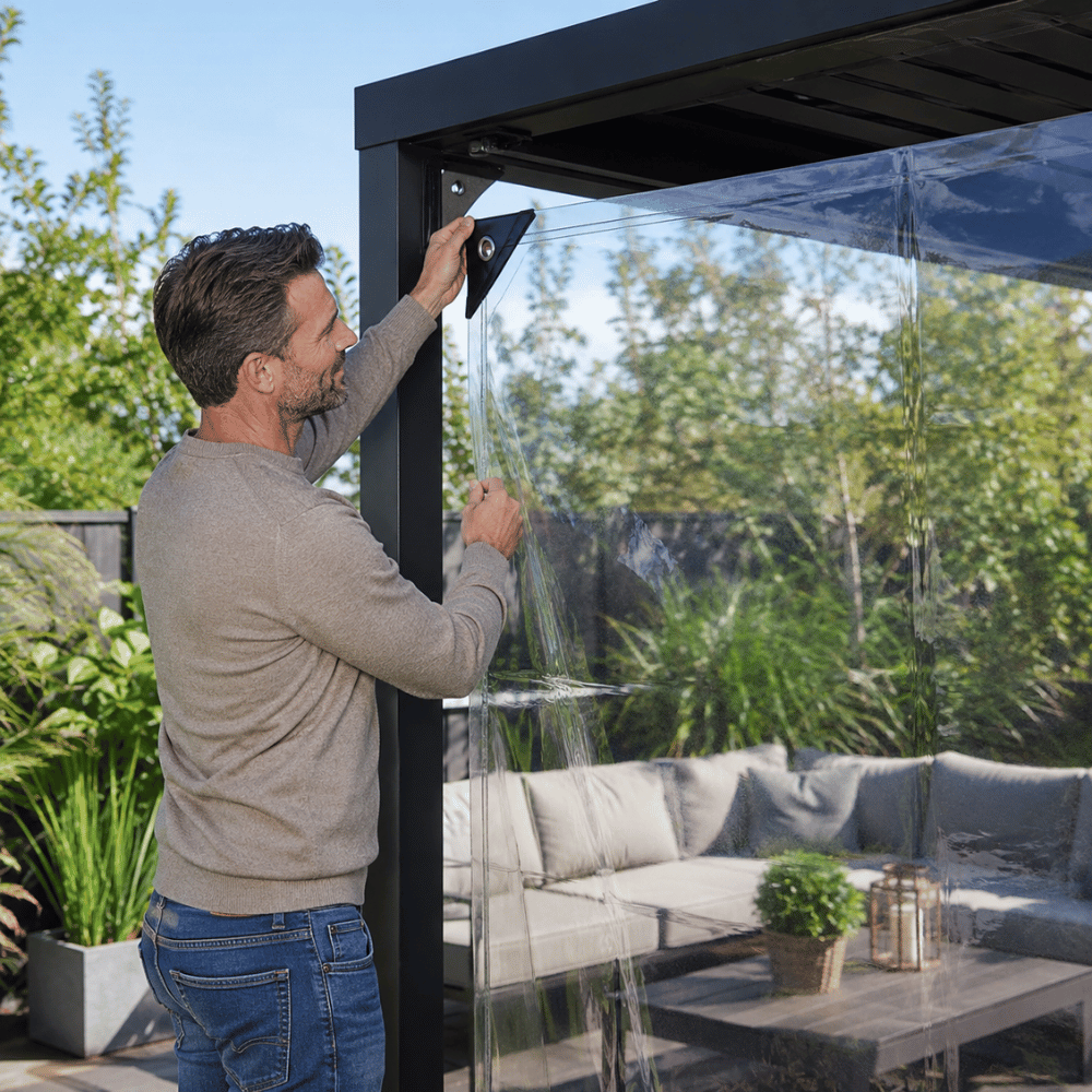 Homme accrochant une bâche transparente sur le côté d'une pergola
