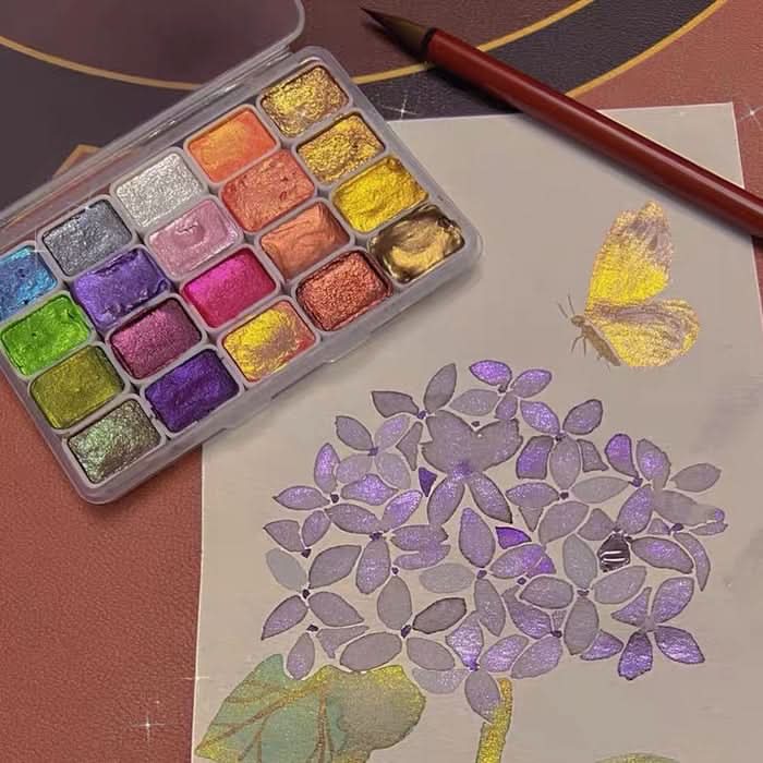 Coffret d'aquarelle nacrée ouvert à côté d'un hortensia peint aux reflets violets