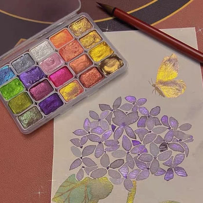 Coffret d'aquarelle nacrée ouvert à côté d'un hortensia peint aux reflets violets